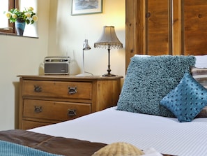 A bedroom with a wooden dresser, a radio, a lamp, and a bed with blue and patterned pillows. - 2 bedroom accommodation in Hartland (Hartland)