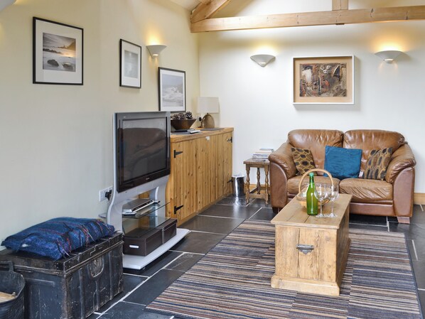 A living room with a television, wooden cabinet, leather sofa, and a coffee table. - 2 bedroom accommodation in Hartland (Hartland)