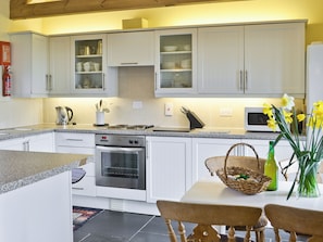 A modern kitchen with white cabinets, a built-in oven, a microwave, and a dining area with a table and chairs.