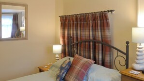 A bed with a plaid blanket, a pillow, a bedside lamp, and a nightstand with a lamp. - 2 bedroom accommodation in Pen-y-Sarn, near Amlwch (Pen-y-Sarn, near Amlwch)