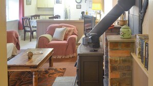 A cozy living room with a fireplace, a dining area, and a kitchen in the background. - 2 bedroom accommodation in Pen-y-Sarn, near Amlwch (Pen-y-Sarn, near Amlwch)
