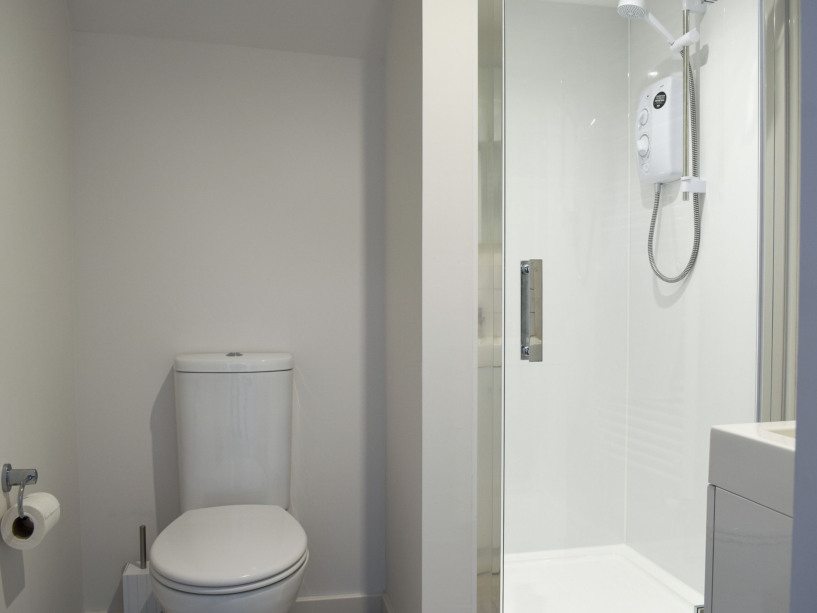 Une salle de bain moderne équipée de toilettes, d’une douche et d’un porte-rouleau de papier toilette.