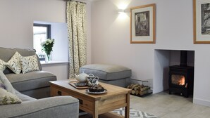 A cozy living room with a sofa, a table with a teapot and a plate of food, a fireplace, and a window with curtains. - 3 bedroom accommodation in Muthill, near Crieff (Muthill, near Crieff)