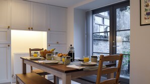 A kitchen with white cabinets, a wooden table, and a window with a view of a stone wall. - 3 bedroom accommodation in Muthill, near Crieff (Muthill, near Crieff)