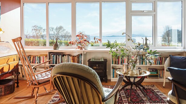 Ein gemütliches Wohnzimmer mit Seeblick, ein Schaukelstuhl, ein Bücherregal und ein Kamin.