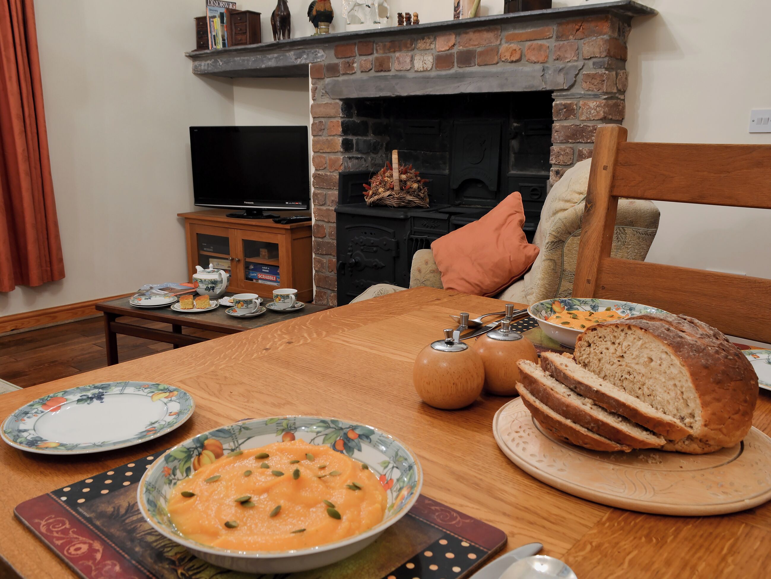 Un coin repas avec une table en bois dressée pour le repas, une cheminée et un téléviseur en arrière-plan.