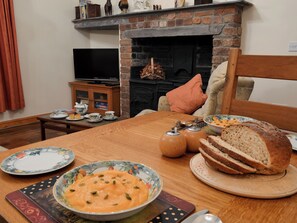 Ein Essbereich mit Holztisch, gedecktem Tisch für eine Mahlzeit, einem Kamin und einem Fernseher im Hintergrund.