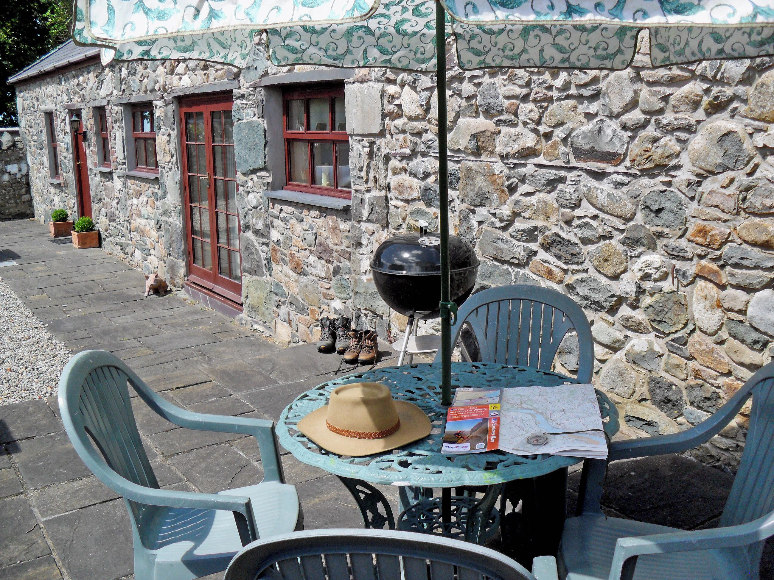 A stone building with a rustic exterior, a barbecue grill, and outdoor seating with chairs and a table.