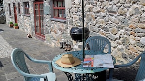 A stone building with a rustic exterior, a barbecue grill, and outdoor seating with chairs and a table.