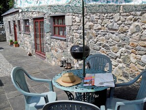 Ein Steinhaus mit rustikalem Äußeren, einem Grill und einer Sitzgruppe mit Stühlen und Tisch.