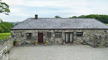Une maison en pierre avec une allée en gravier et une cour clôturée.
