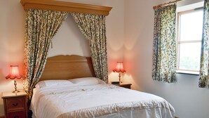 A bedroom with a large bed, two bedside tables with lamps, floral curtains, and a window with curtains.