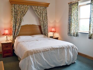 Ein Schlafzimmer mit einem großen Bett, zwei Nachttischen mit Lampen, floralen Vorhängen und einem Fenster mit Vorhängen.