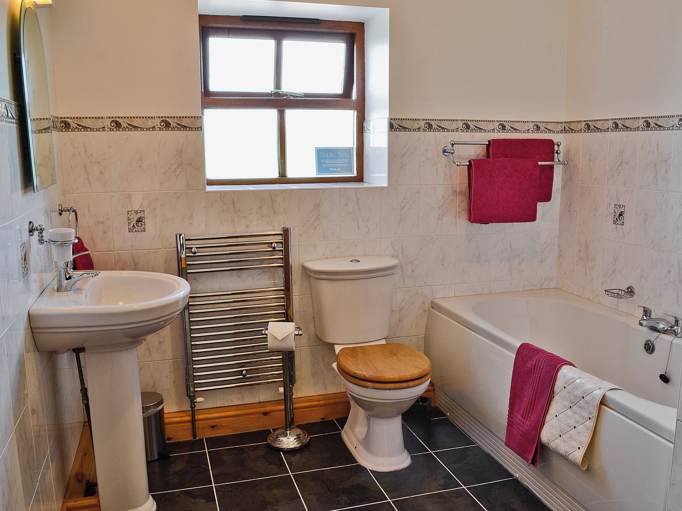 A bathroom with a sink, toilet, and bathtub, featuring a window and tiled walls.