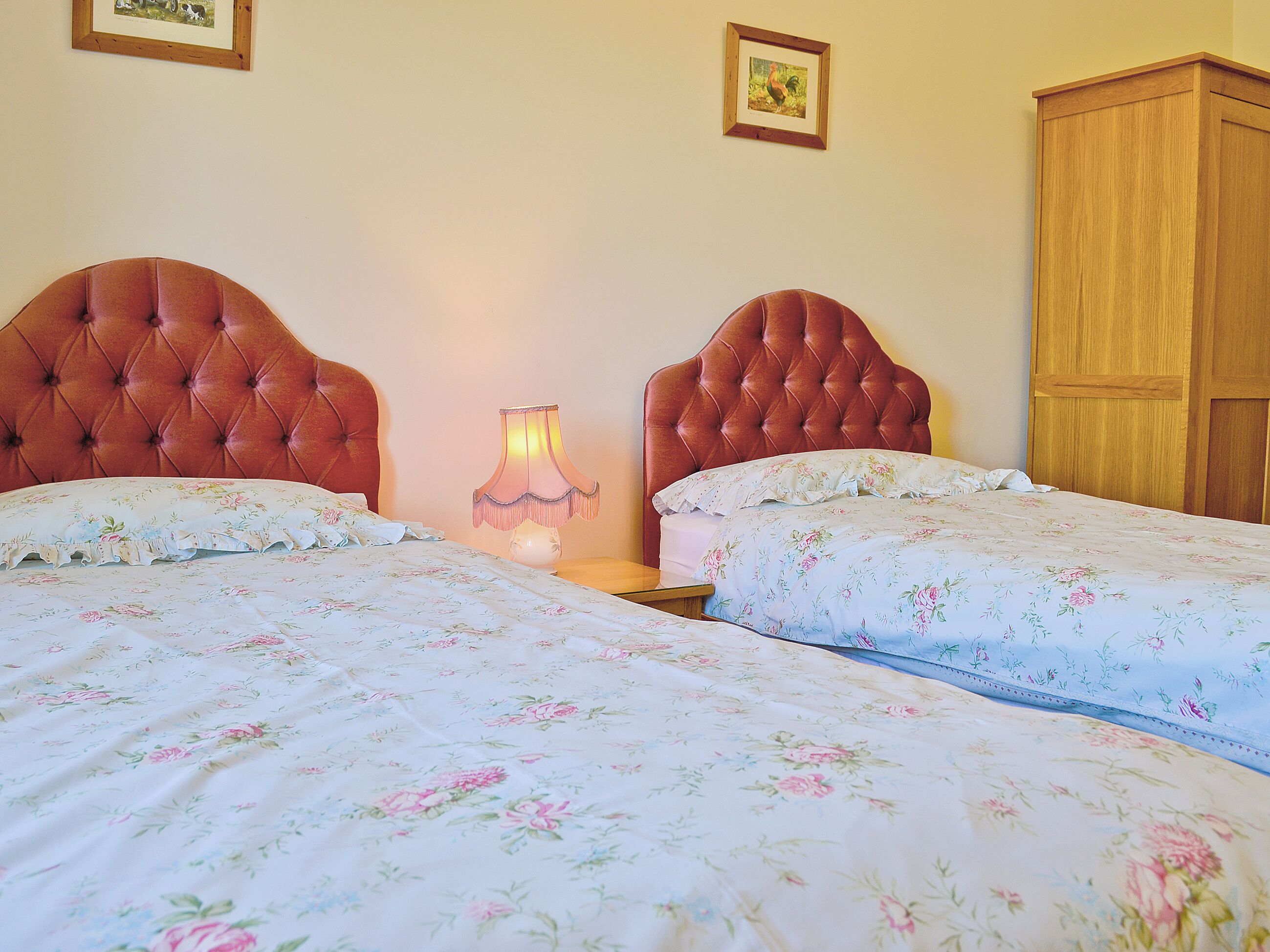 Une chambre avec deux lits, une table de chevet, une lampe et une armoire en bois.