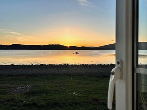 A view of a lake at sunset with a boat on the water, a grassy shore, and a mountain range in the background. - 3 bedroom accommodation in Taynuilt (Taynuilt)