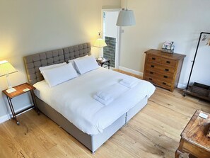 A neatly made bed with white linens, a wooden nightstand with a lamp, a dresser with drawers, and a door leading to a balcony. - 3 bedroom accommodation in Taynuilt (Taynuilt)
