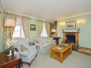 A living room with a sofa, armchair, wooden coffee table, fireplace, bookshelves, and a lamp.