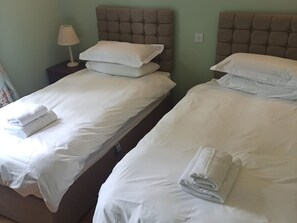 Two twin beds with white linens and pillows, a bedside lamp, and a green wall. - 3 bedroom accommodation in Taynuilt (Taynuilt)