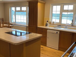 A kitchen with a central island, wooden cabinets, a dishwasher, and a view of a lake through large windows.