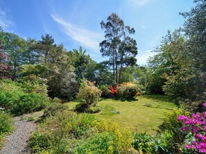 Un jardin où l’on trouve une variété de plantes et d’arbres, un chemin de gravier et une pelouse.