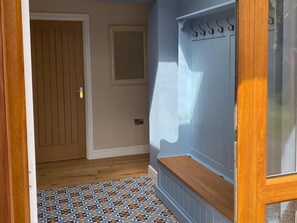 Un couloir avec un sol à motifs, une porte en bois et un mur blanc orné d’une petite fenêtre.