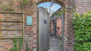 A narrow brick alleyway leading to a wooden gate with a sign indicating 'Coach House'.