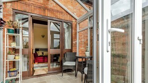 A cozy patio area with a brick wall, a sliding glass door leading to an interior space with a red sofa and wicker chairs.