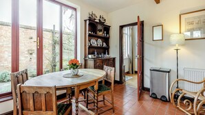 A dining area with a wooden table and chairs, a vase with flowers, a brick wall, and a window with a view of the outside.