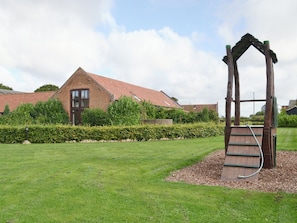 Une zone herbeuse avec une structure en bois et, au fond, un bâtiment en briques.