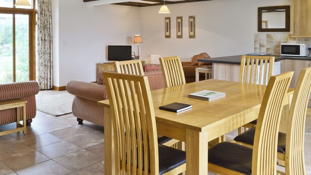 A dining area with a wooden table and chairs, a television, and a kitchen area with a microwave. - 3 bedroom accommodation in Catfield (Catfield)
