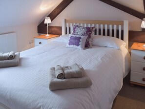 Een keurig opgemaakt bed met opgerolde handdoeken, een houten hoofdbord en twee nachtkastjes met lampen.