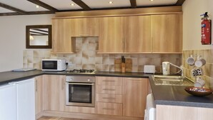 A compact kitchen with wooden cabinets, a microwave, a toaster, and a gas stove. - 3 bedroom accommodation in Catfield (Catfield)