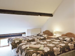 Une chambre avec deux lits, une tête de lit en bois, une table de chevet avec une lampe et une fenêtre donnant sur un paysage verdoyant.