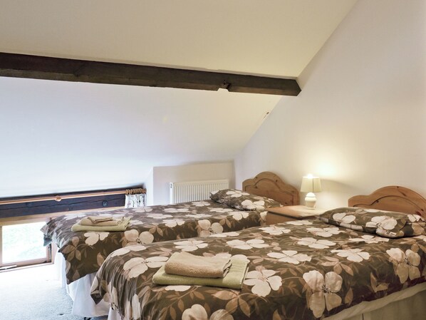 A bedroom with two beds, a wooden headboard, a nightstand with a lamp, and a window with a view of greenery.