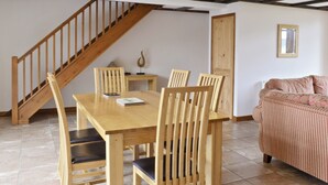 A dining area with a wooden table and chairs, a staircase, and a sofa. - 3 bedroom accommodation in Catfield (Catfield)