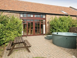 A brick building with a large glass door, a wooden bench, and a hot tub.