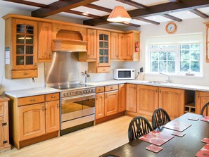 Cocina con armarios de madera, electrodomésticos de acero inoxidable, microondas y un comedor con sillas y mesa.