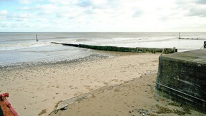 A beach with a wooden jetty extending into the sea, a rocky shoreline, and a cloudy sky. - Beach Retreat - E5558 (Mundesley)