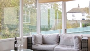 A wicker sofa with cushions, a glass table with a magazine, and a bottle of wine. - Beach Retreat - E5558 (Mundesley)