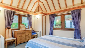 Un dormitorio con cama, cómoda, silla y ventanas con cortinas.