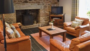 A living room with a stone fireplace, leather sofas, a television, and a fireplace log storage. - 4 bedroom accommodation in St Blazey, near Par (St Blazey, near Par)