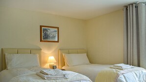 Une chambre d’hôtel avec deux lits, une table de chevet avec une lampe, un tableau au mur et une fenêtre avec des rideaux.