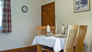 Un coin repas avec une table en bois dressée pour deux personnes, une horloge et un tableau encadré accroché au mur.