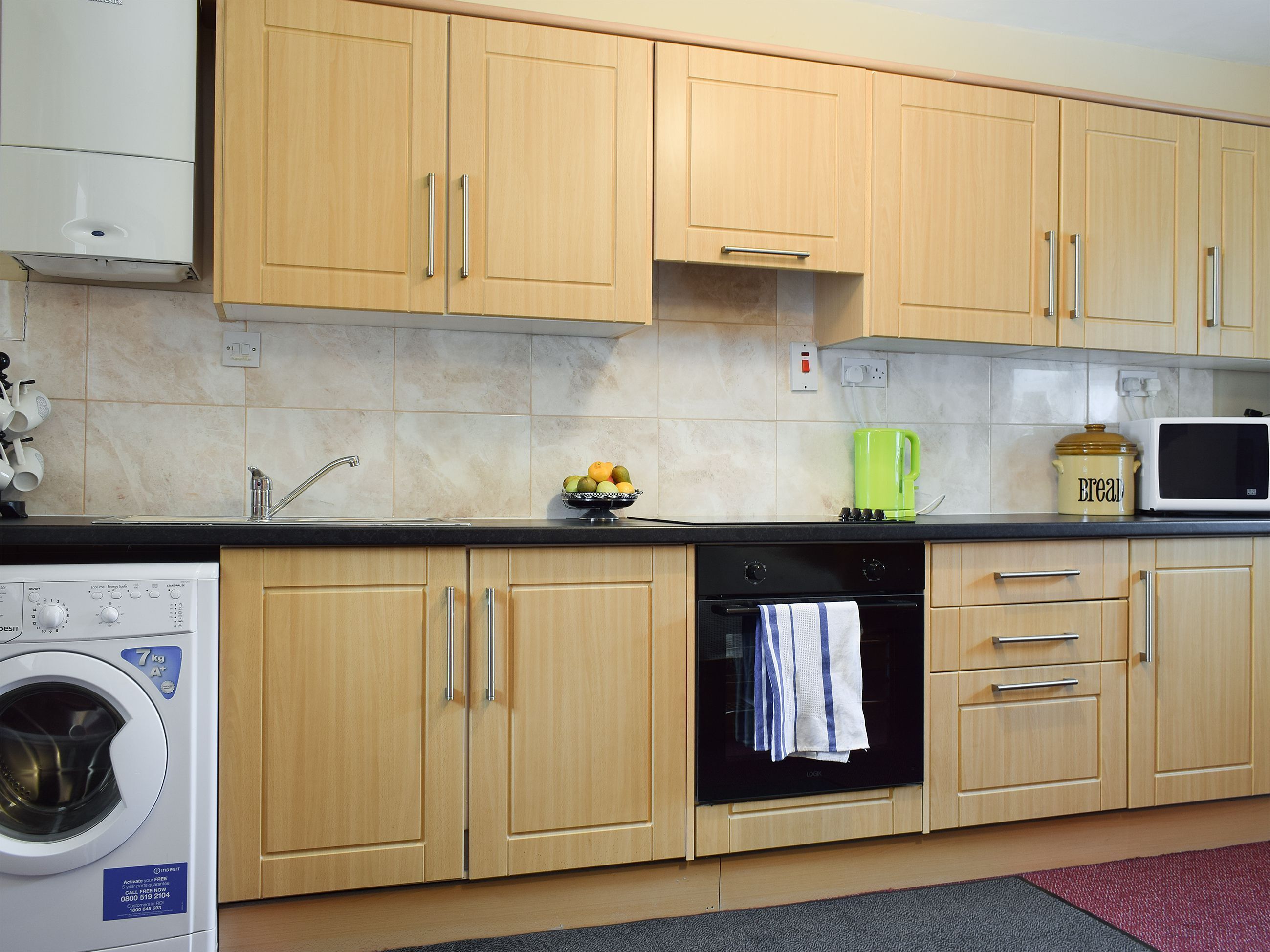A kitchen with wooden cabinets, a washing machine, an oven, and a microwave.