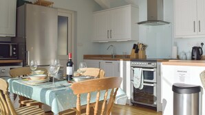 Una cocina con una mesa de comedor para cuatro personas, un refrigerador, un horno y un microondas.