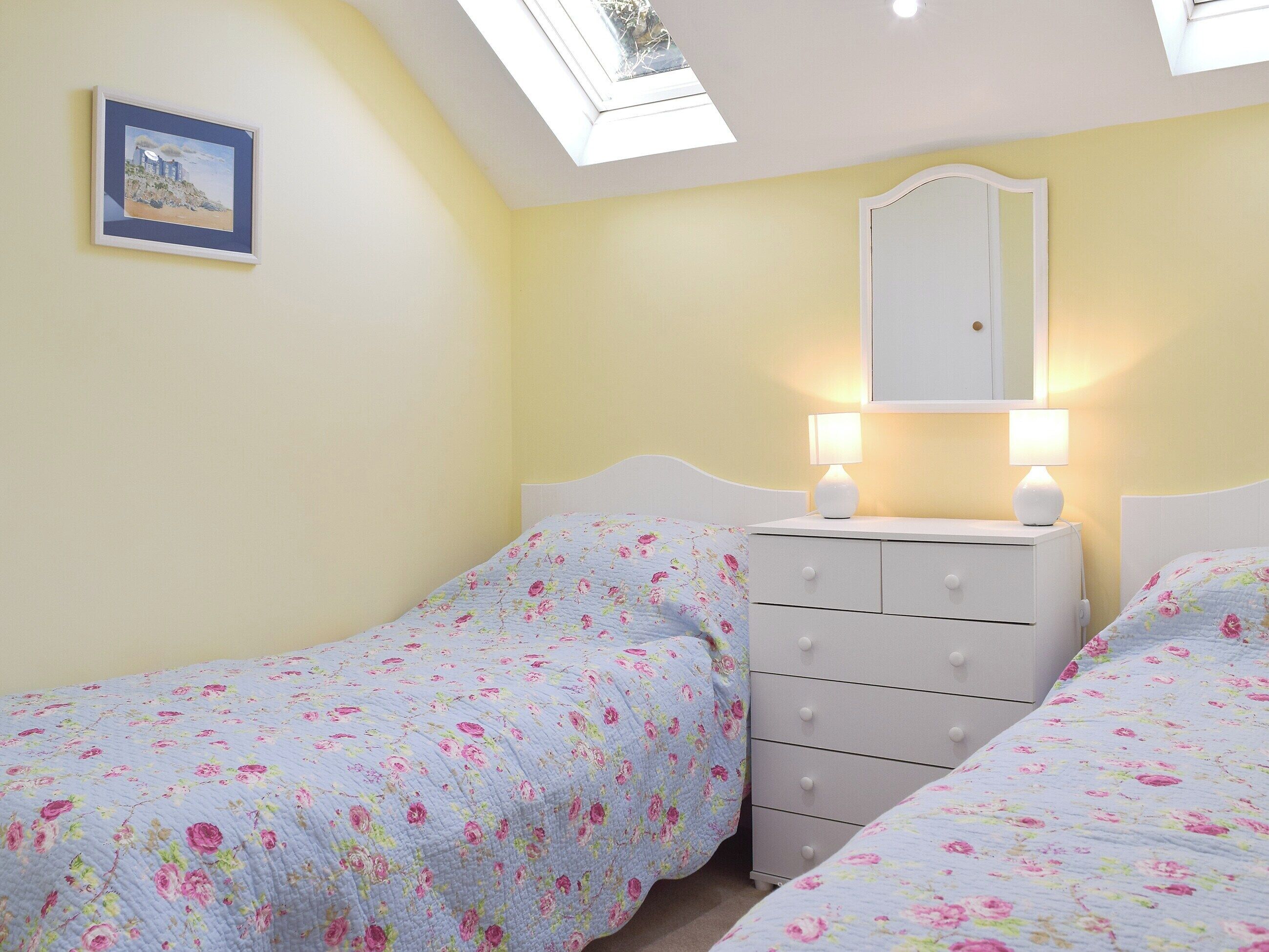 A bedroom with two beds, a dresser, a mirror, and a skylight.