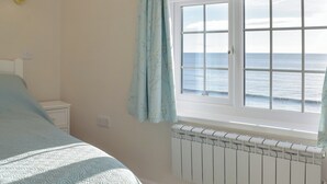 Un dormitorio con cama, mesita de noche, ventana con vista al mar y lámpara de pared.