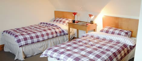 A bedroom with two beds, each with a plaid bedspread, a wooden headboard, and a nightstand with a lamp.