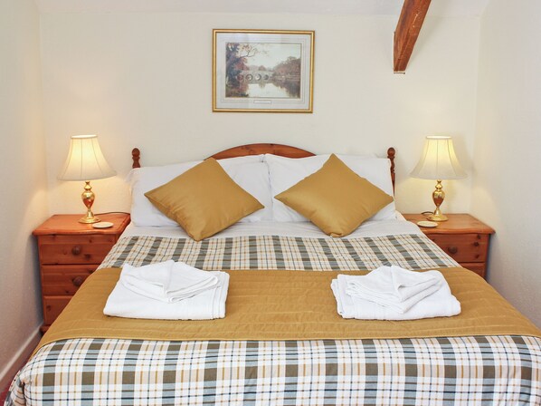 A neatly made bed with a plaid bedspread, two pillows, two bedside tables with lamps, and a framed picture on the wall.